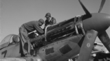A black and white photo of two airmen working on a propeller-driven airplane